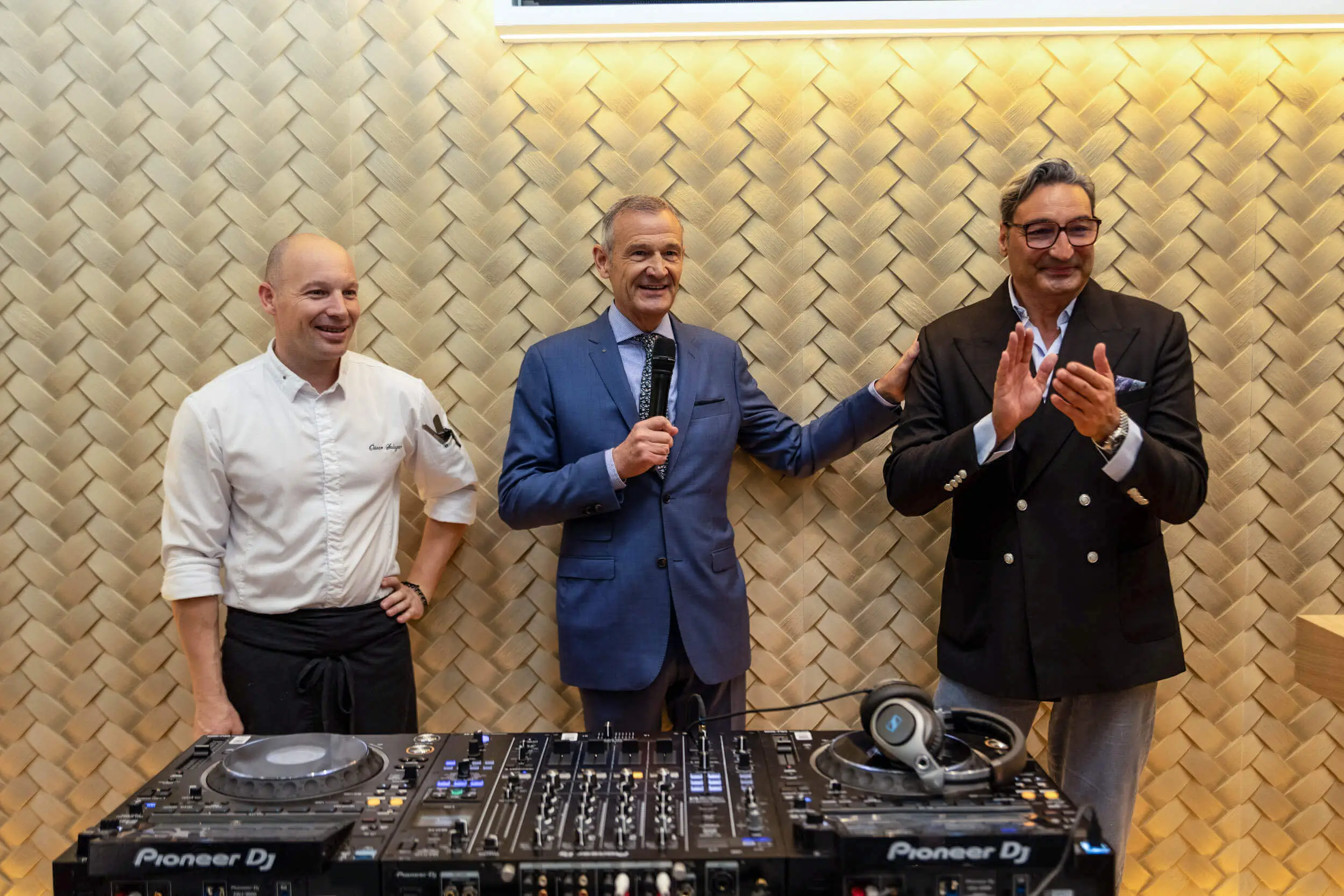 Drei Männer bei einem Event vor einem DJ-Mischpult.