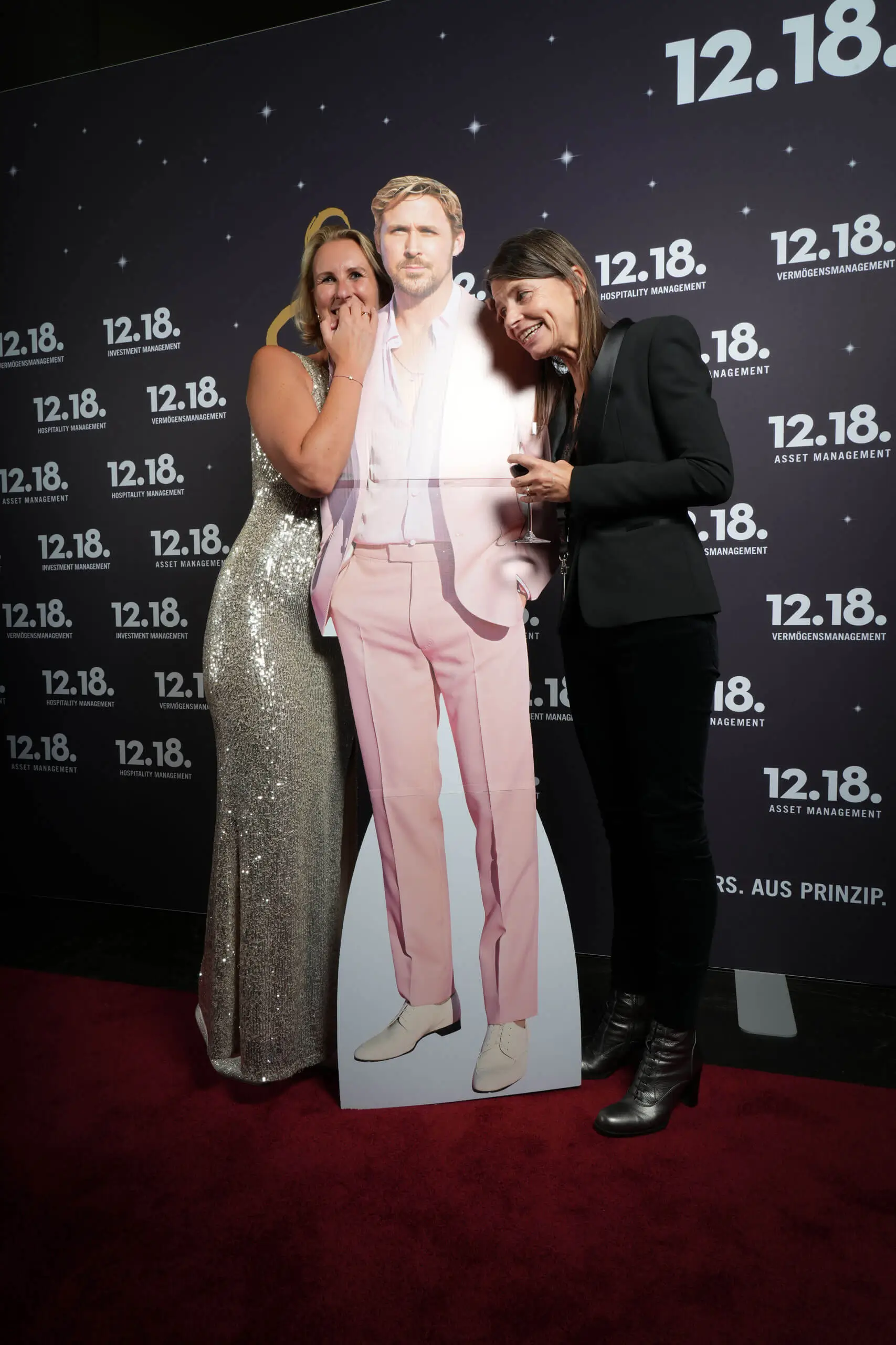Frauen lachen mit einem Lebensgroßen Cutout von Ryan Gosling auf einer Veranstaltung.