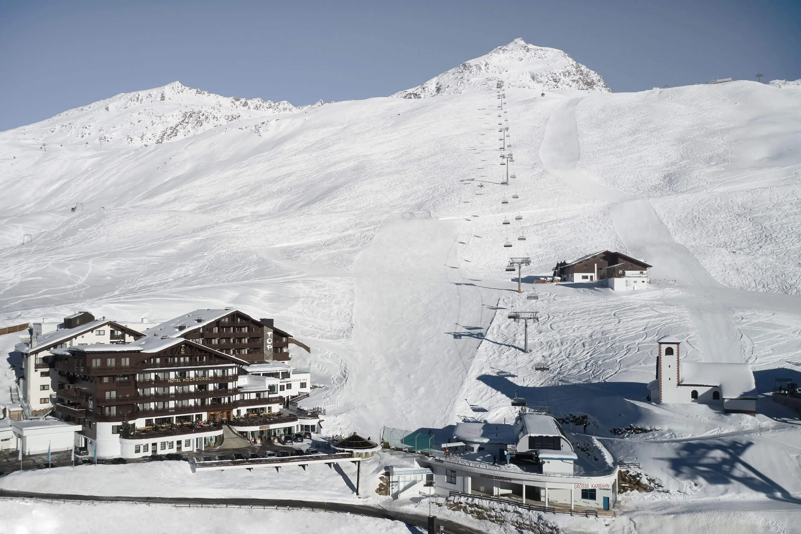 Malersicher Blick auf ein verschneites Skigebiet mit Gebäuden und Skiliften unter blauem Himmel.