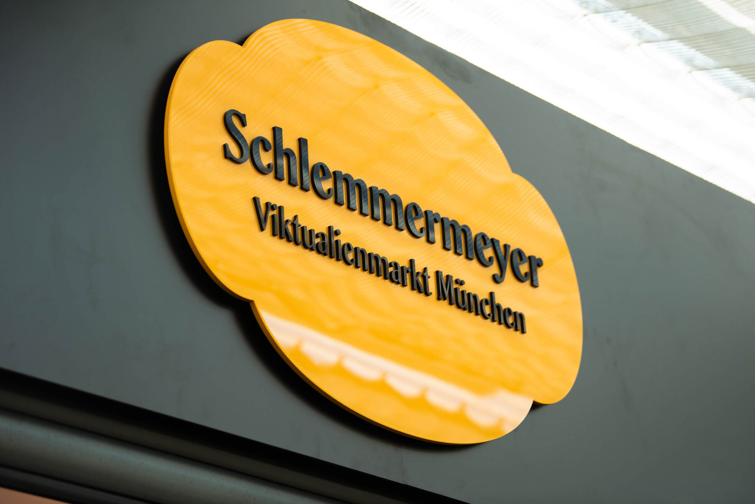 Ein gelbes Schild an einer grauen Wand mit der Aufschrift Schlemmermeyer und Viktualienmarkt Münche