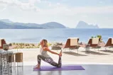 Frau praktiziert Yoga mit Blick auf das Meer und die Berge.